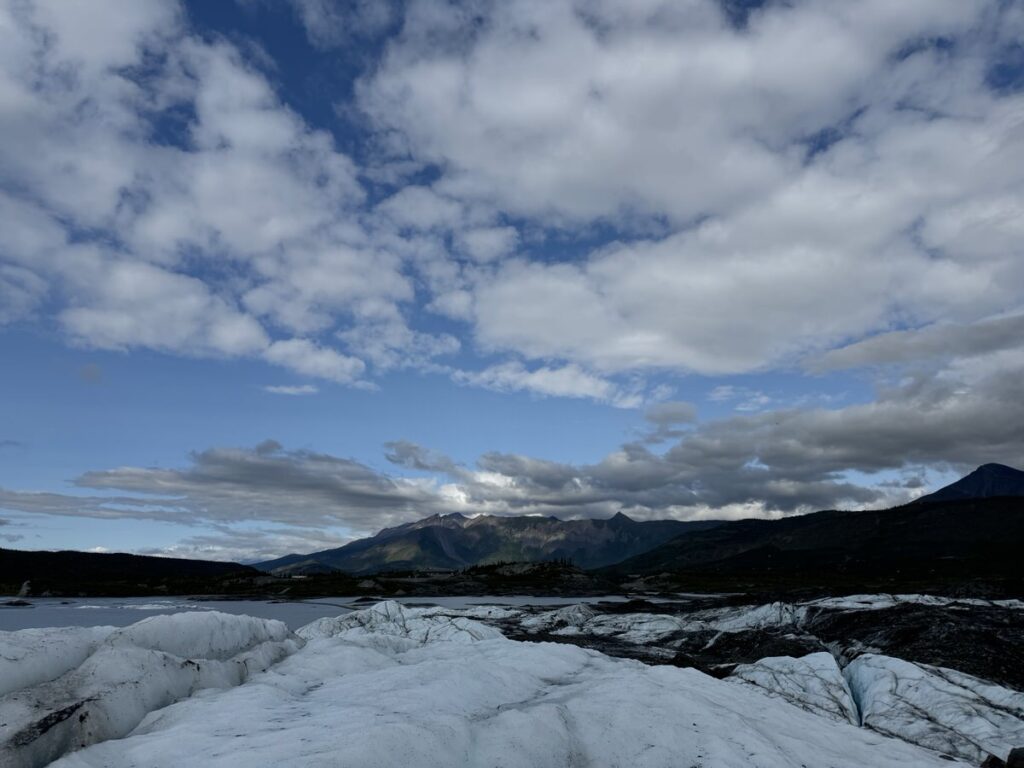 Snow-covered landscape in the foreground with distant mountains under a partly cloudy sky, capturing the serene beauty often found on Alaska hikes.