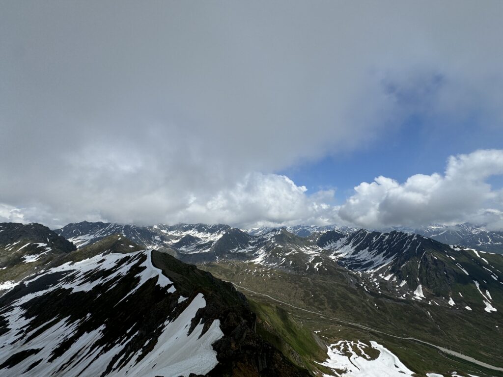 Mountain range with snow patches on the slopes under a partly cloudy sky, with peaks visible in the distance—an inspiring scene often encountered on Alaska hikes.