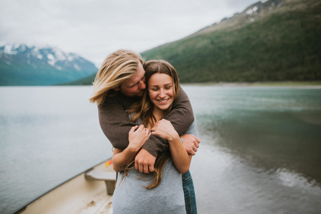 Couple hugging on lake shore with mountain backdrop, 
