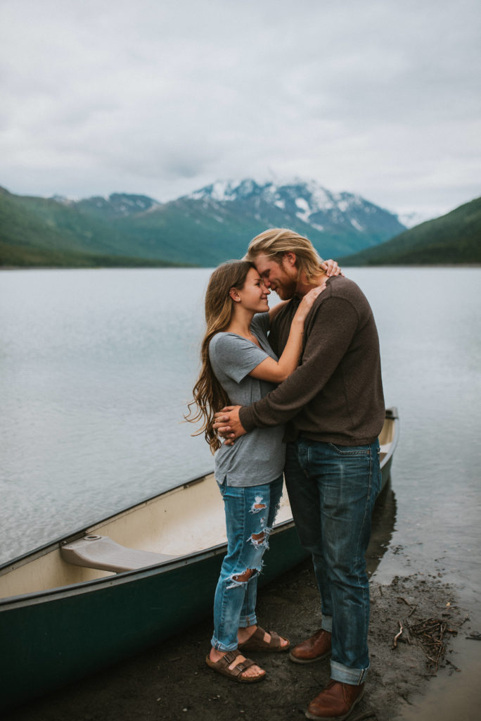 Couple hugging on lake shore with mountain backdrop, 